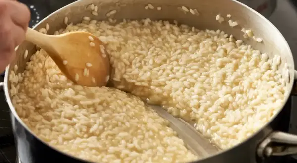 Gotuje się kremowy ryż do risotto w garnku, mieszany drewnianą łyżką.