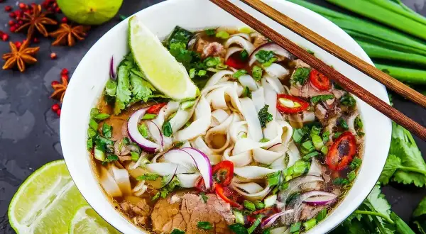 Aromaticzny makaron pho z wołowiną, świeżą kolendrą, cebulą i chili. Podany z limonką i pałeczkami.