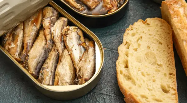 Otwarta puszka ryb wędzonych, obok kromki chleba. Czy ryby wędzone a cholesterol to temat do dyskusji?
