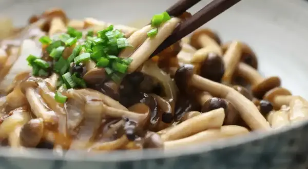 Chopsticks podnoszą pyszne, duszony chińskie grzyby, posypane zieloną cebulką.