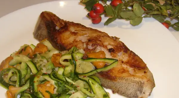Złocisty halibut stek z chrupiącą skórką, podany z sałatką z cukinii i kurkami.