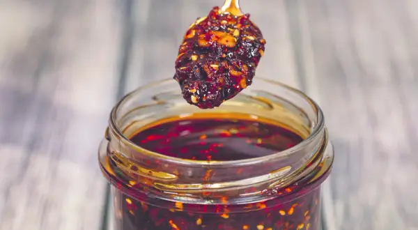 Łyżeczka z aromatycznym chili w oleju nad słoikiem pełnym tej pikantnej przyprawy.