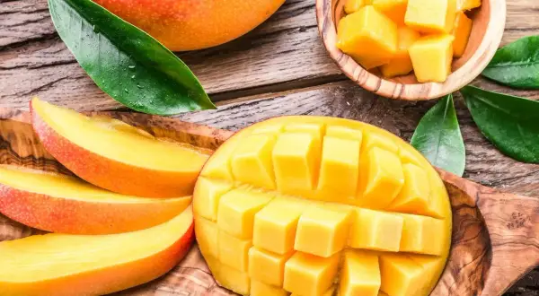 Soczyste, pokrojone w kostkę i plastry mango, które pokazuje, co to jest mango. Całe, dojrzałe owoce i liście na drewnianym tle.