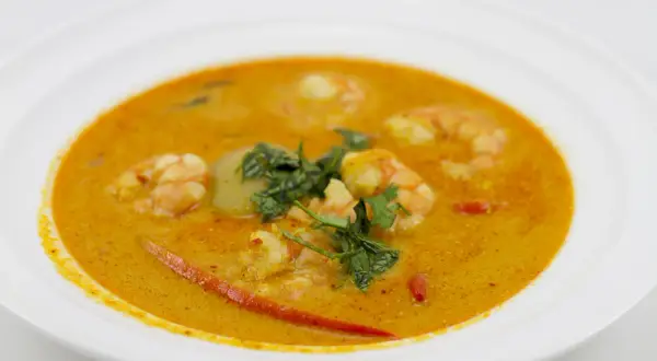 Aromatyczna zupa tom yum z krewetkami, ozdobiona świeżą kolendrą i kawałkami chili, podana w białej misce.