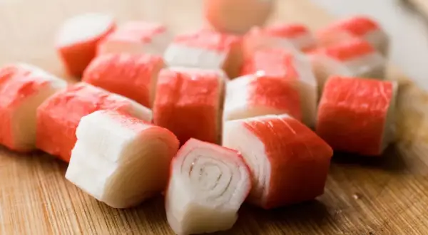 Pokrojone paluszki surimi na desce. Idealne do sałatek i przekąsek.