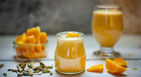 Słodki jogurt z mango, udekorowany kawałkami owoców, obok miseczki z mango i kardamonu.
