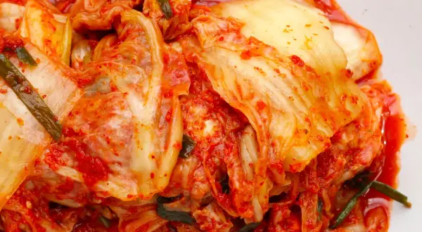 Pikantna kapusta kimchi, z widocznymi liśćmi i przyprawami, gotowa do podania.