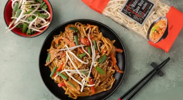 Chow mein z kurczakiem, warzywami i kiełkami fasoli mung, obok opakowania makaronu i miseczki z kiełkami. Idealne danie z wykorzystaniem przypraw chińskich.