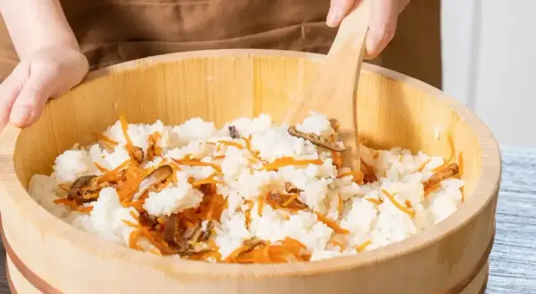 Mieszanie ryżu z marchewką i grzybami w drewnianej misce, przygotowanie zaprawy do sushi.