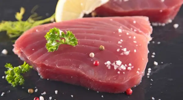 Świeży tuńczyk filet, doprawiony solą i pieprzem, z plasterkiem cytryny i natką pietruszki. Gotowy do grillowania.
