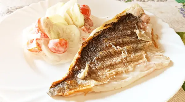 Dorada grillowana z chrupiącą skórką, podana z orzeźwiającą sałatką z pomidorków i ogórka w sosie.