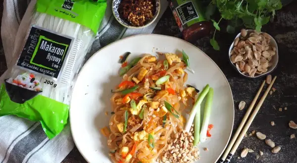 Pyszny pad thai z wołowiną, makaronem ryżowym i orzeszkami ziemnymi. Obok składniki: makaron, sos i płatki chili.