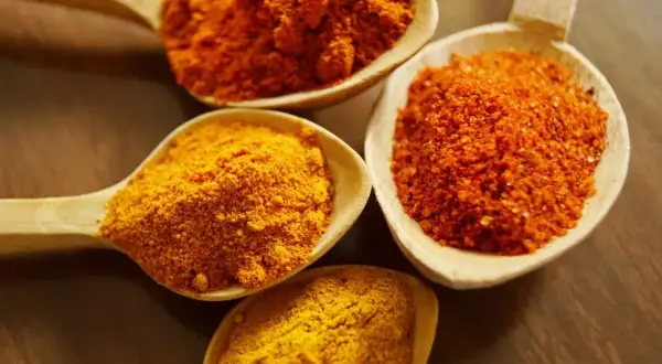 Drewniane łyżki wypełnione przyprawami: intensywnie żółta kurkuma i pomarańczowe proszki, idealne do aromatycznego curry.
