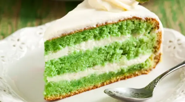Zielone ciasto z matcha i mascarpone, przełożone kremem, ozdobione bitą śmietaną i truskawką.