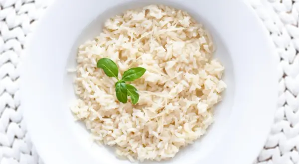 Ryż parboiled co to? Gotowany ryż z parmezanem i listkiem bazylii na białym talerzu.