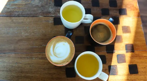 Kawa i herbata na drewnianym stole. Czy zielona herbata pobudza? Obok kawy latte i czarnej, dwie filiżanki z zieloną herbatą.