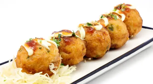 Pięć złotych kulek takoyaki, polanych majonezem i sosem, na białym talerzu z poszatkowaną kapustą. Idealne japońskie przekąski, przepisy na nie są proste!