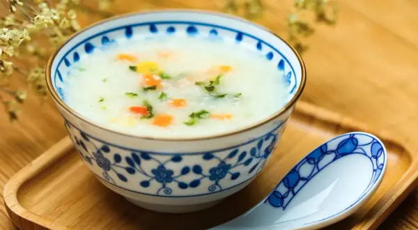 Misternie zdobiona miseczka z congee, czyli tradycyjną azjatycką owsianką z warzywami. Obok leży łyżka.