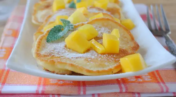 Puszyste placuszki z cukrem pudrem i kostkami mango, ozdobione listkami mięty. Idealne śniadanie z mango.