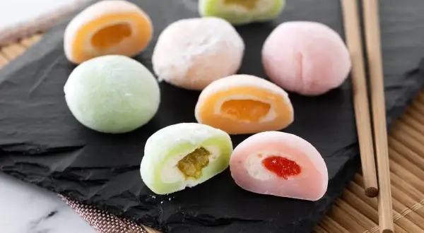 Kolorowe mochi z owocowym nadzieniem, idealne do domowego przepisu na mochi. Patyczki do jedzenia obok.