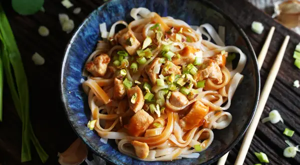 Miseczka makaronu ryżowego z kurczakiem, posypana szczypiorkiem i orzechami, w sosie Pad Thai.