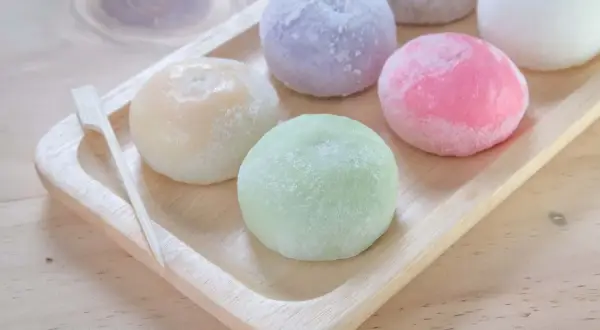 Kolorowe japońskie lody mochi na drewnianej tacy, wyglądają jak małe, słodkie kuleczki.