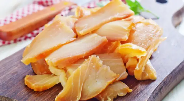 Kawałki złocistych ryb wędzonych, ułożone na drewnianej desce. Różne rodzaje ryb wędzonych kuszą apetycznym wyglądem.