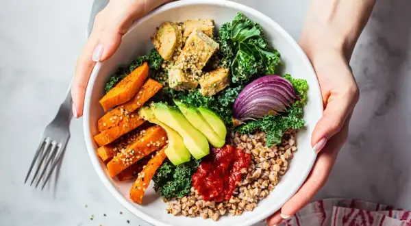 Zdrowy bowl z kaszą gryczaną, pieczonymi batatami, awokado, tofu, jarmużem i czerwoną cebulą.