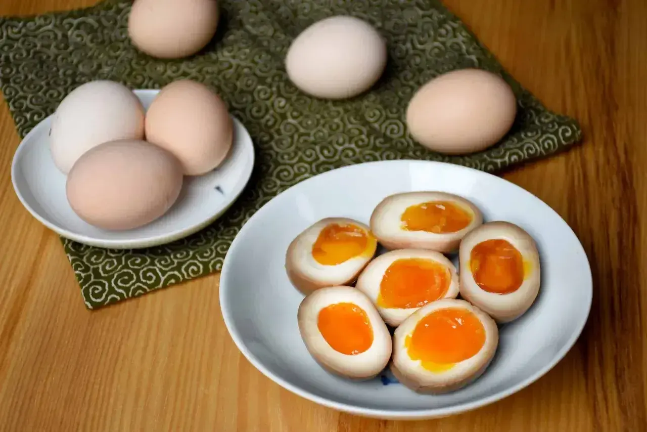 Na talerzu leżą przekrojone na pół marynowane jajka z płynnym, pomarańczowym żółtkiem. Obok kilka całych jajek.