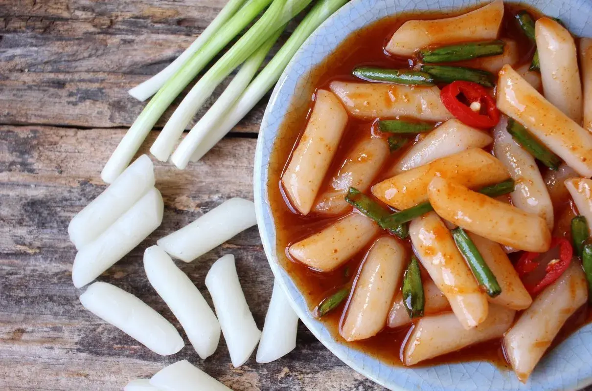Pyszne kluski ryżowe tteokbokki w pikantnym sosie, podane z dymką i papryczką chili.
