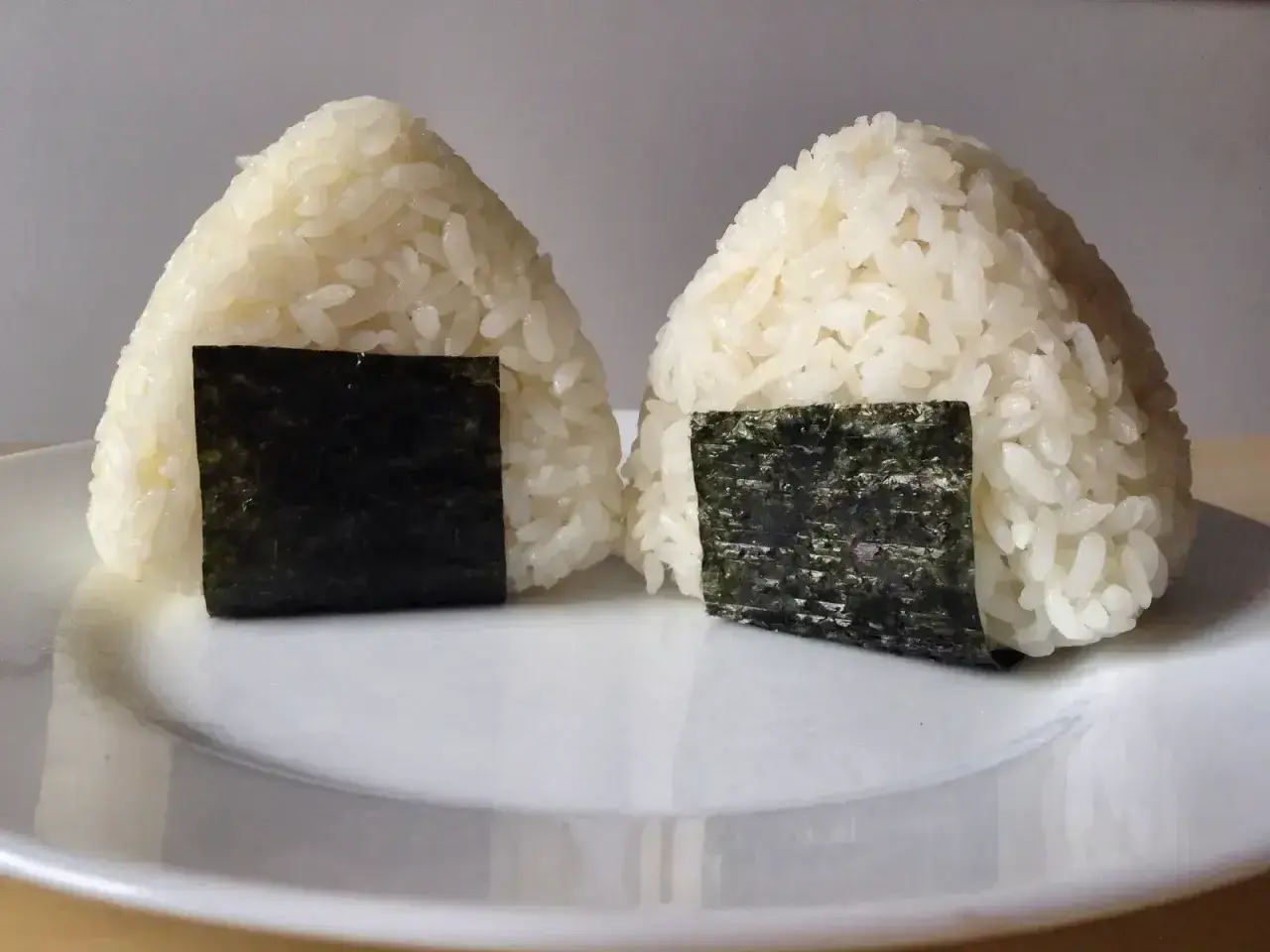 Dwa japońskie kulki ryżowe, onigiri, z kawałkami nori na białym talerzu.