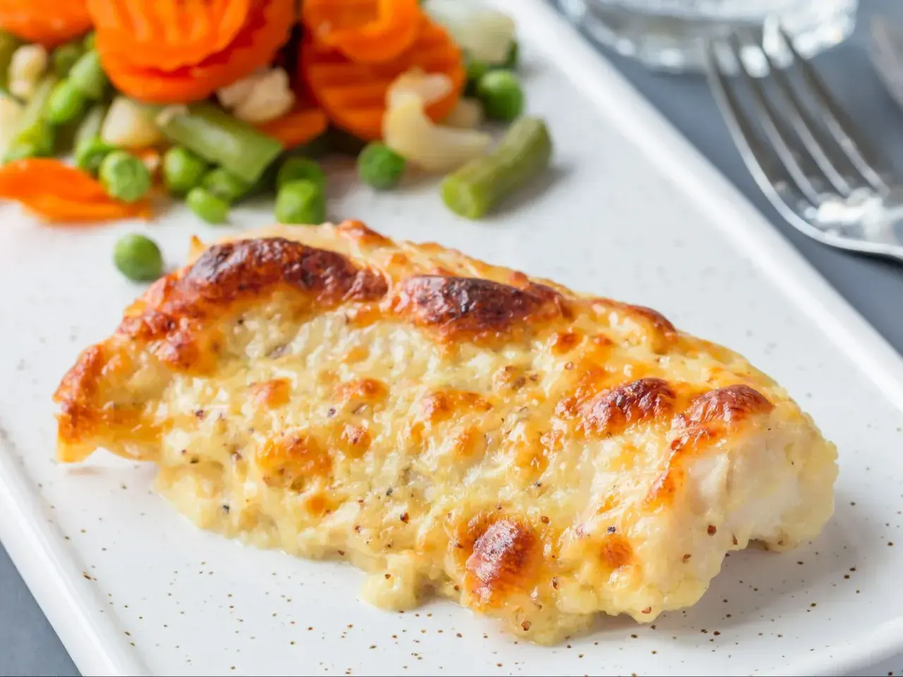 Pyszny, zapieczony filet z dorsza w sosie serowym, podany z kolorowymi warzywami.