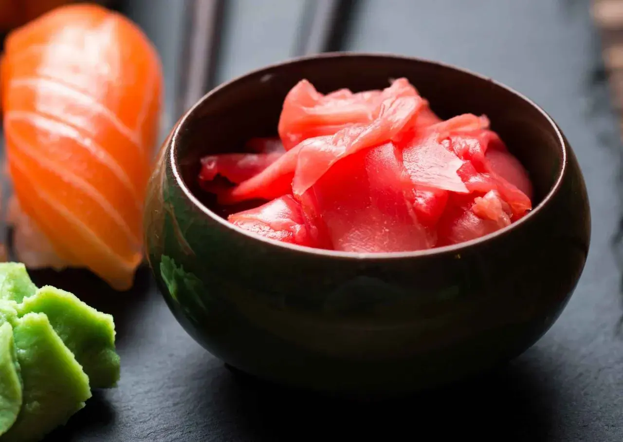 Miseczka z różowym, marynowanym imbirem obok sushi z łososiem i zielonym wasabi.