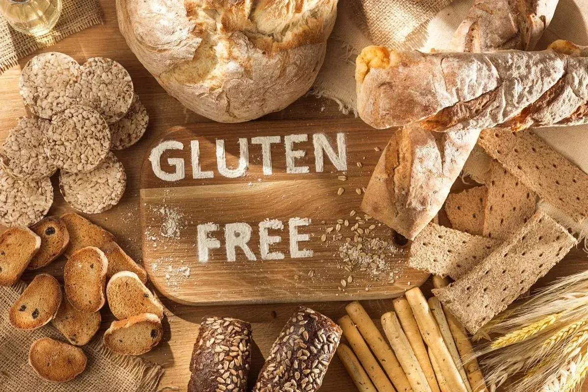 Różnorodne pieczywo i przekąski, na desce napis "GLUTEN FREE". Dowiedz się, co to jest gluten i jak go unikać.