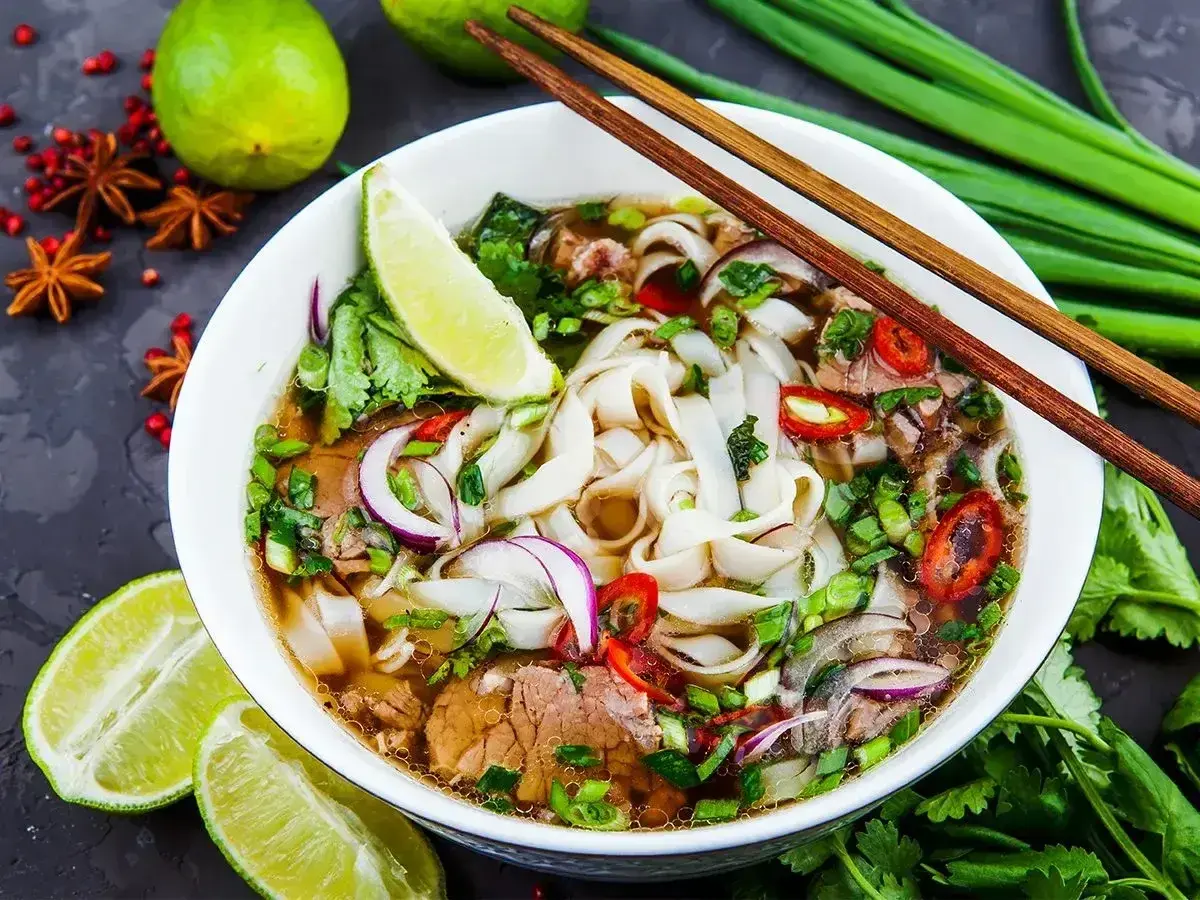 Aromaticzny makaron pho z wołowiną, świeżą kolendrą, cebulą i chili. Podany z limonką i pałeczkami.