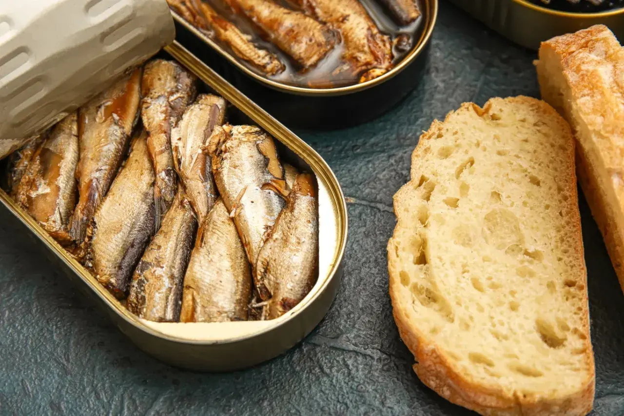Otwarta puszka ryb wędzonych, obok kromki chleba. Czy ryby wędzone a cholesterol to temat do dyskusji?