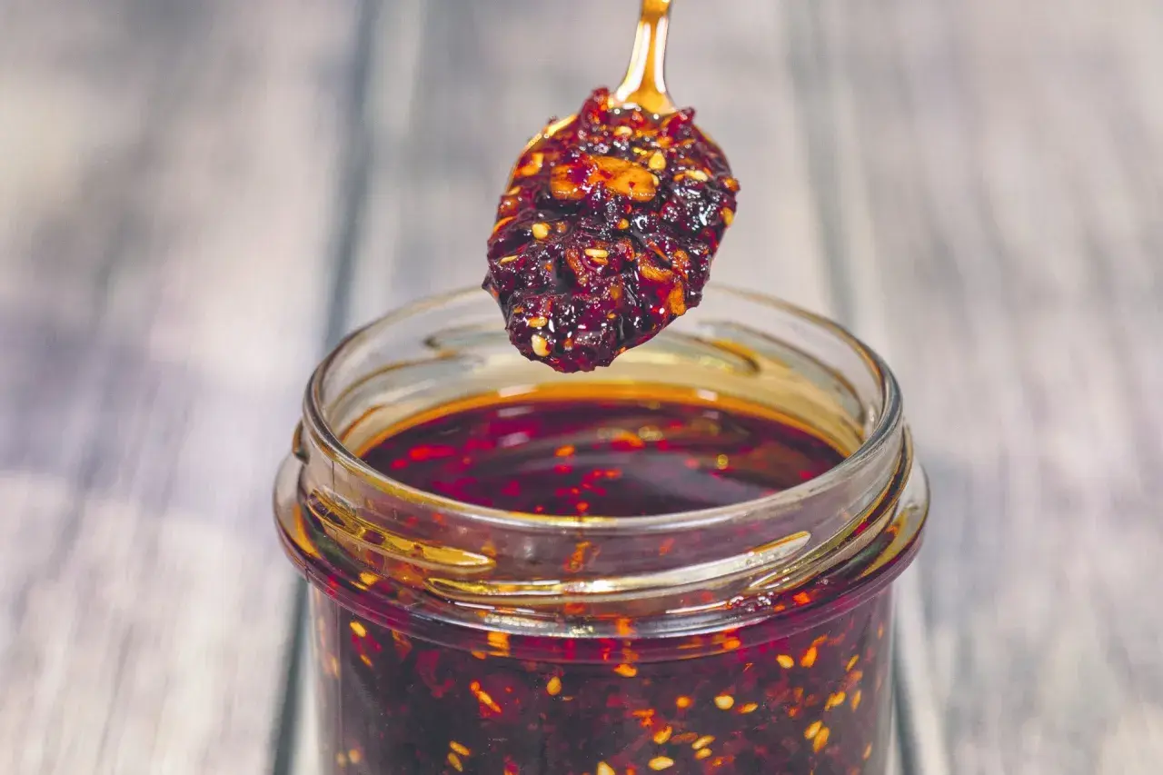 Łyżeczka z aromatycznym chili w oleju nad słoikiem pełnym tej pikantnej przyprawy.