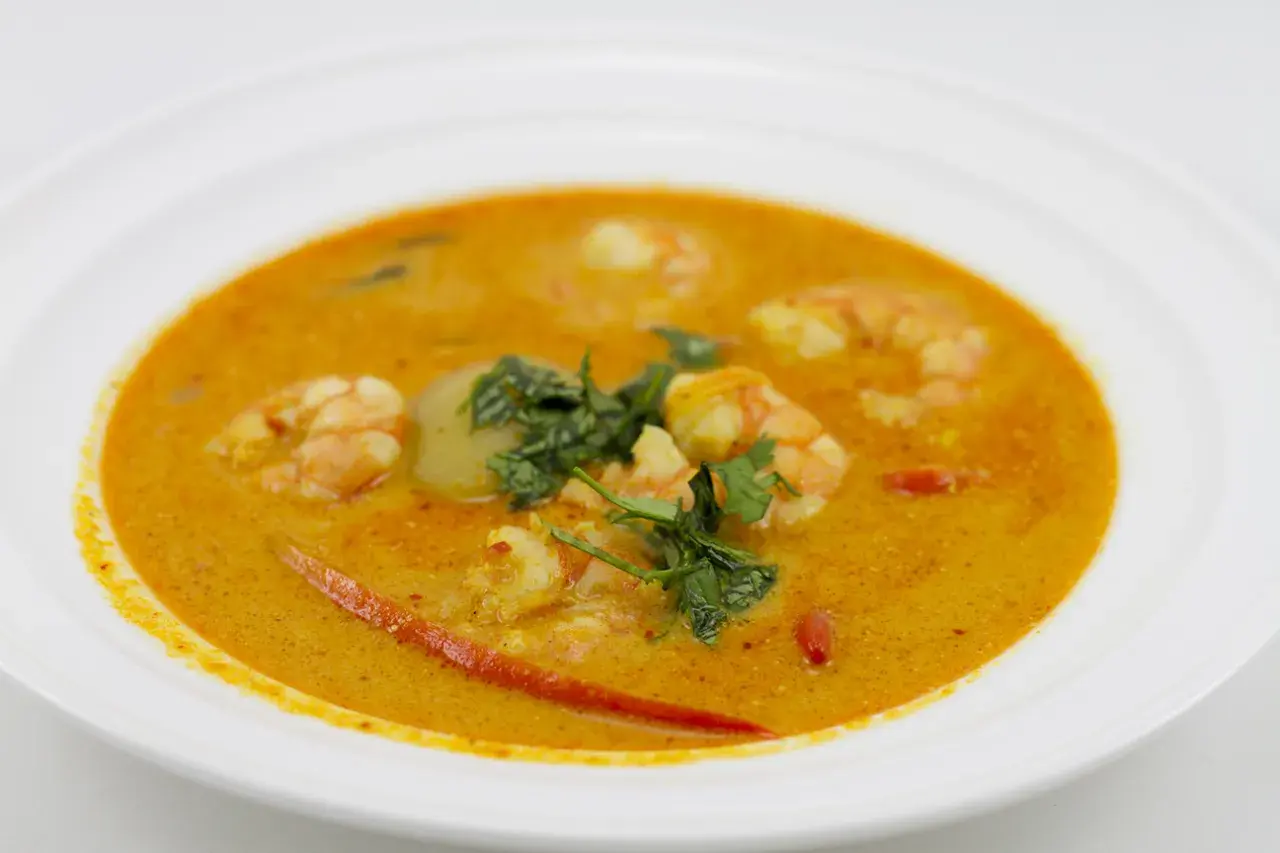 Aromatyczna zupa tom yum z krewetkami, ozdobiona świeżą kolendrą i kawałkami chili, podana w białej misce.