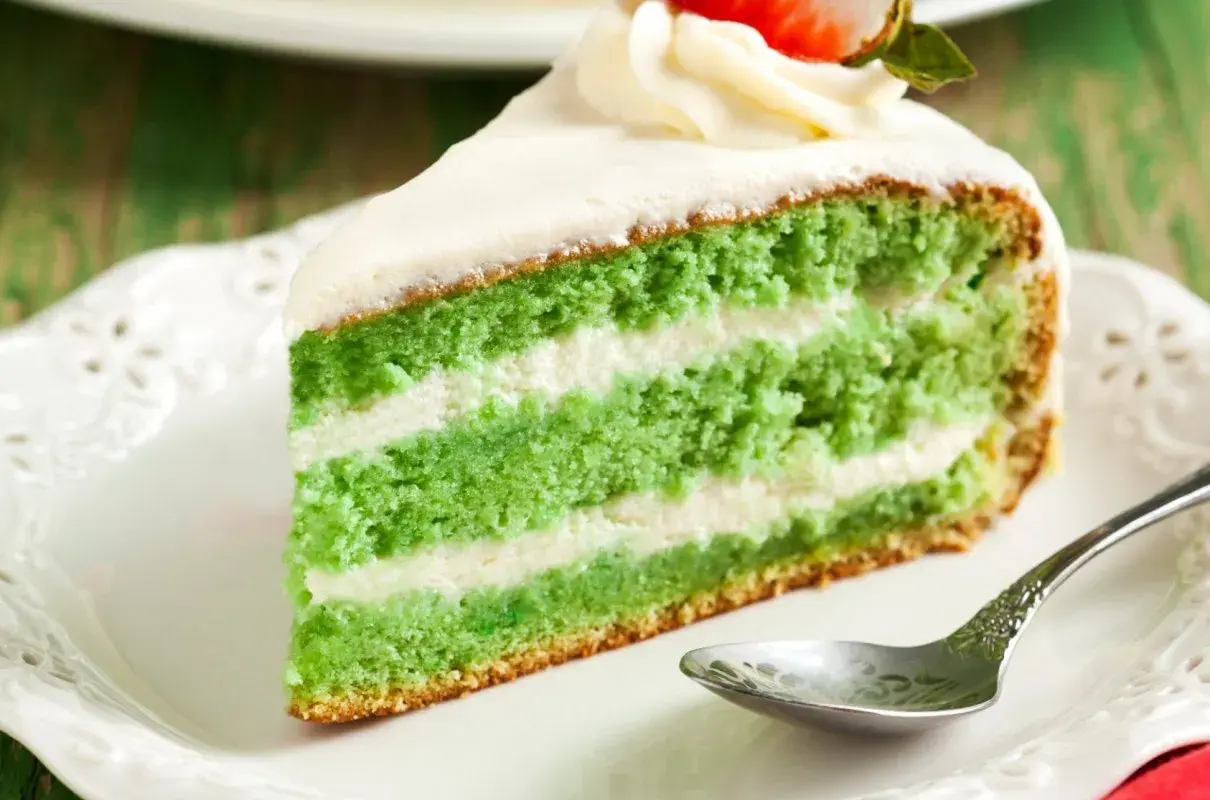 Zielone ciasto z matcha i mascarpone, przełożone kremem, ozdobione bitą śmietaną i truskawką.