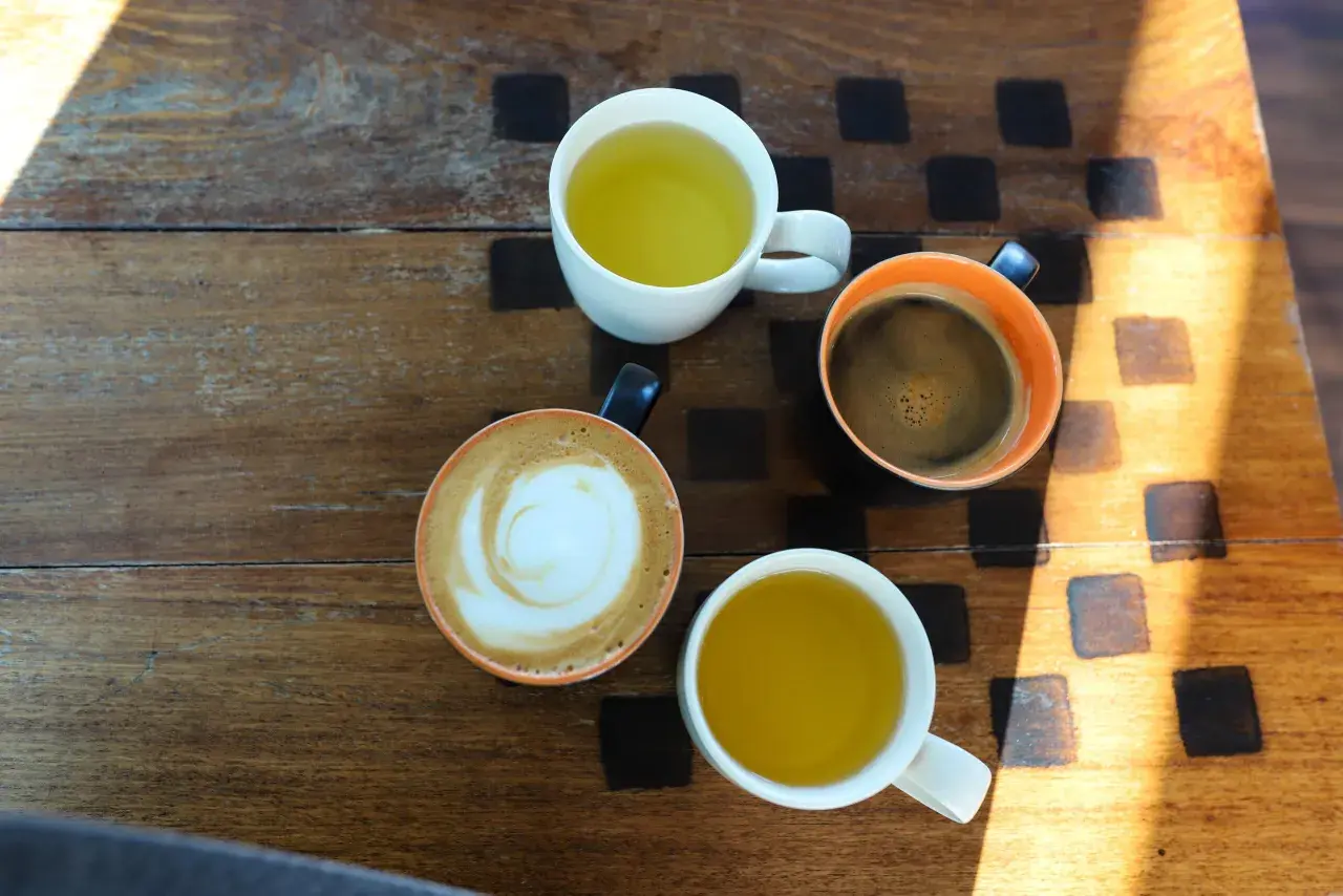 Kawa i herbata na drewnianym stole. Czy zielona herbata pobudza? Obok kawy latte i czarnej, dwie filiżanki z zieloną herbatą.