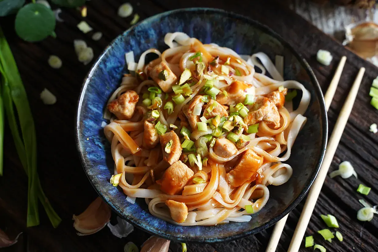 Miseczka makaronu ryżowego z kurczakiem, posypana szczypiorkiem i orzechami, w sosie Pad Thai.