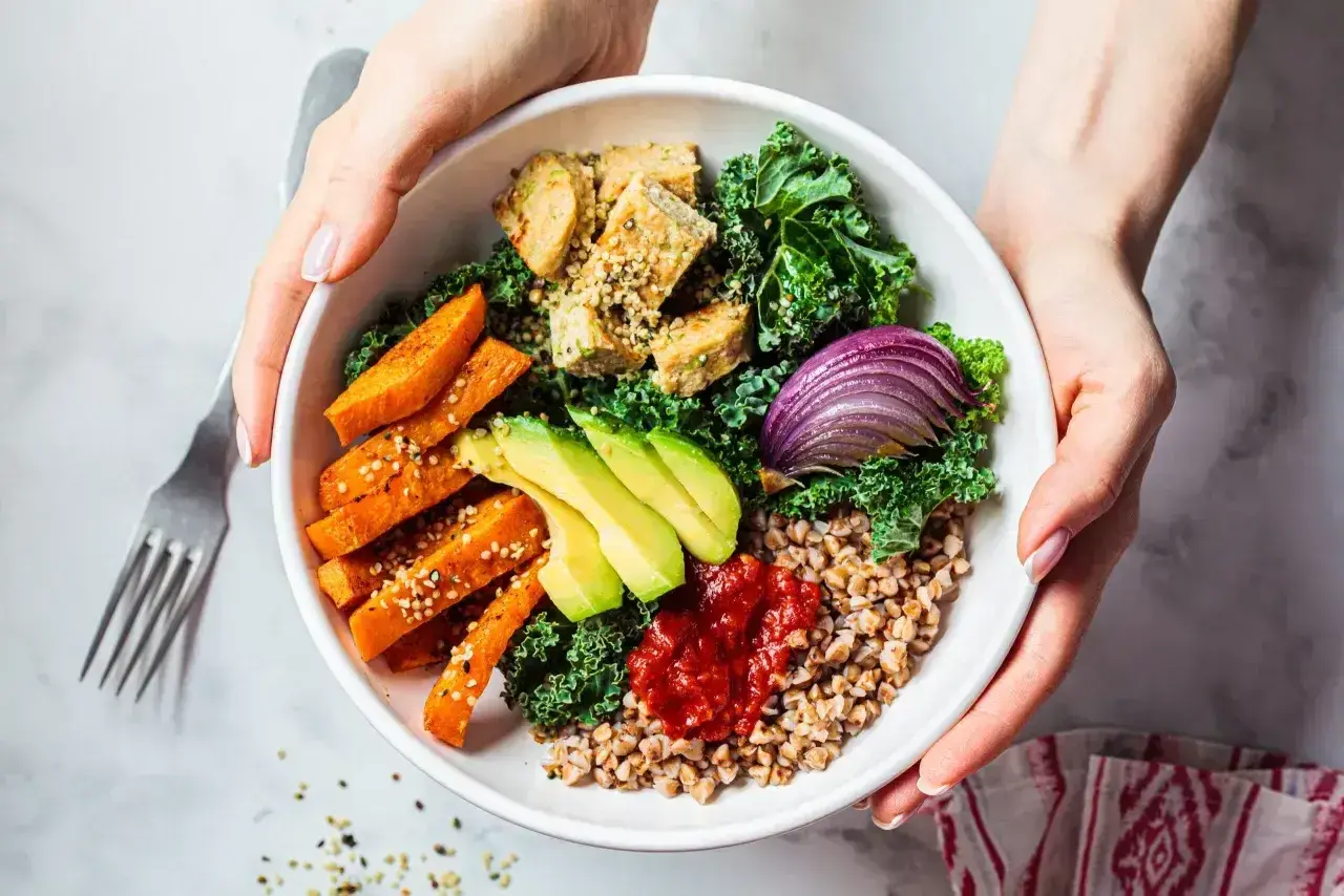 Zdrowy bowl z kaszą gryczaną, pieczonymi batatami, awokado, tofu, jarmużem i czerwoną cebulą.