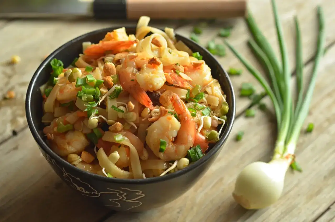 Miseczka pełna krewetek, makaronu ryżowego, kiełków fasoli mung i szczypiorku. To wygląda jak pad thai oryginalny przepis.