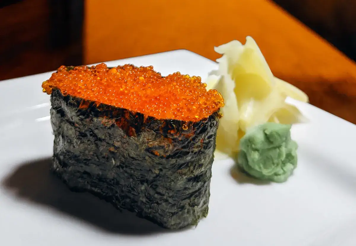 Sushi z ikrą łososia, czyli tobiko. To małe, pomarańczowe kuleczki, które dodają potrawie smaku i tekstury. Obok wasabi i marynowany imbir.