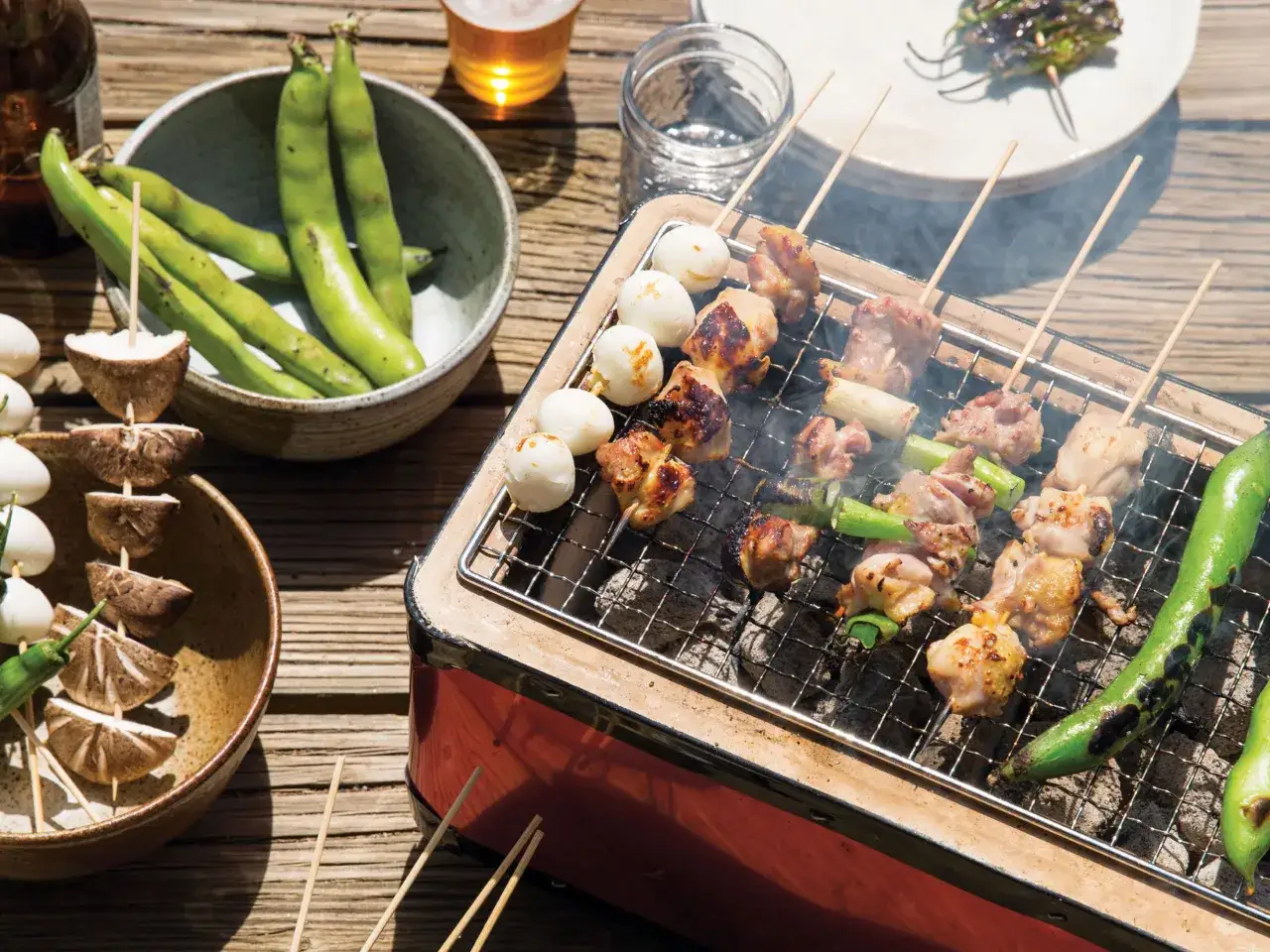 Pyszne yakiniku na grillu: kurczak, przepiórcze jajka i warzywa. Obok miska z fasolką i grzyby na patyczkach.