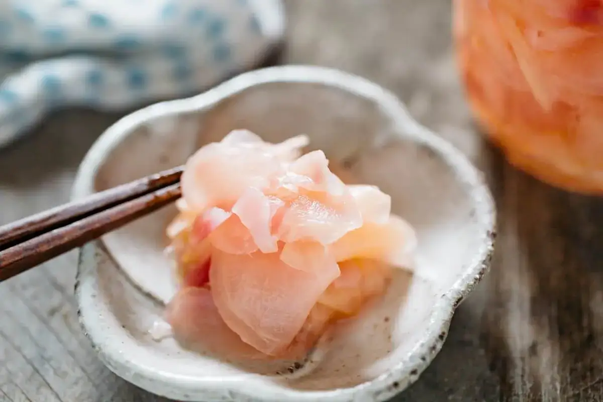 Delikatny imbir marynowany w różowym kolorze, podany w miseczce z pałeczkami. Idealny dodatek do sushi.