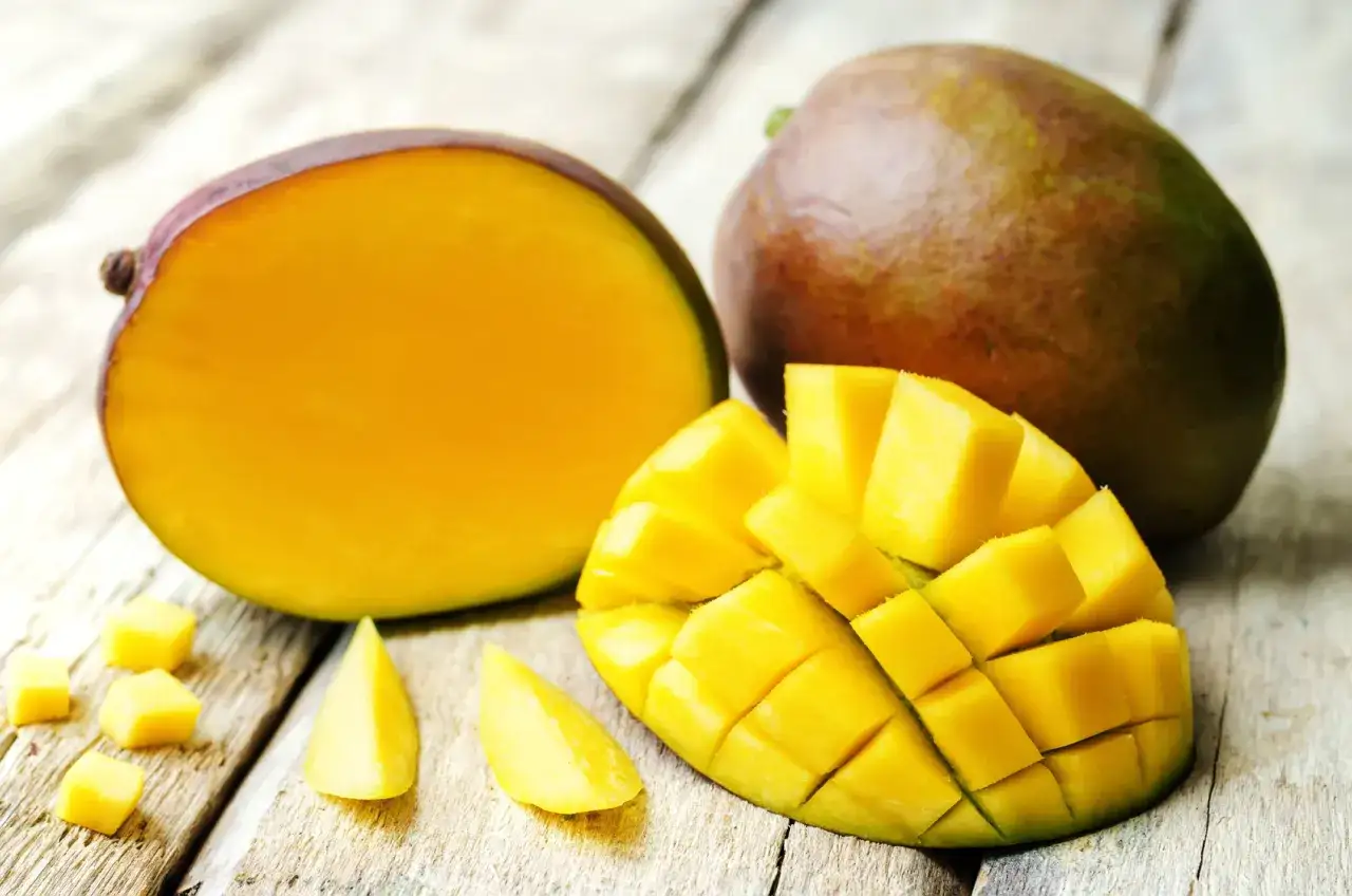 Jak wygląda mango: soczyste, żółte wnętrze, pokrojone w kostkę i na połówki, z całą owocem w tle, na drewnianym blacie.