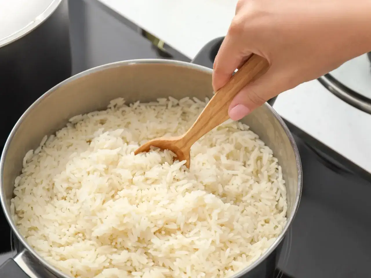 Gotujesz ryż parboiled? To świetny wybór, bo jest sypki i nie skleja się. W garnku widać gotowy, biały ryż, który miesza drewniana łyżka.