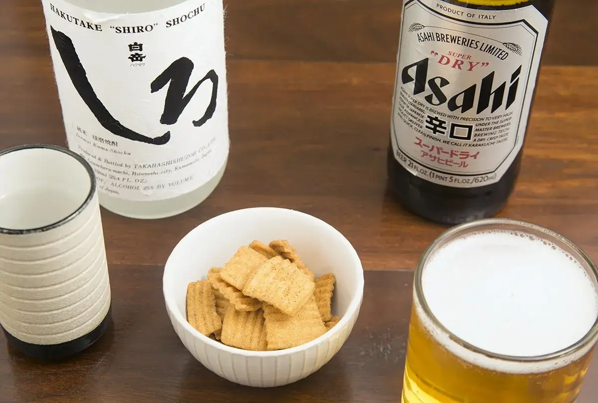 Japońskie piwo Asahi Super Dry obok shochu i miseczki z przekąskami.