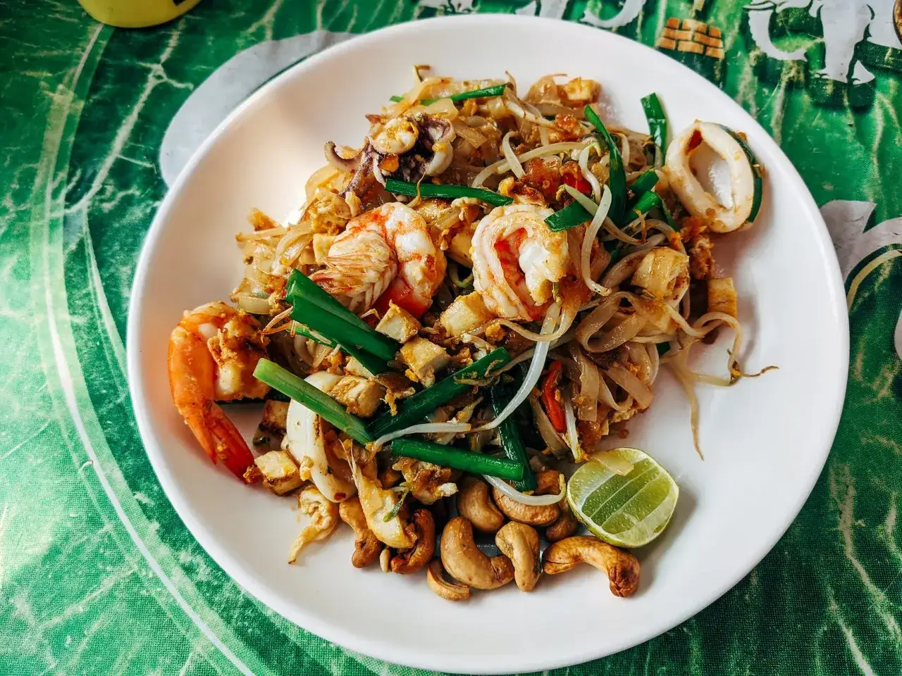 Talerz pełen tajskich przekąsek: Pad Thai z krewetkami, kalmarami, kiełkami fasoli mung, orzechami nerkowca i limonką.